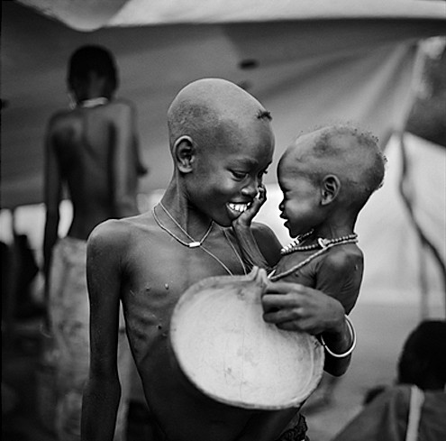 Black-and-white photo of a smiling older child holding a younger child and a large bowl